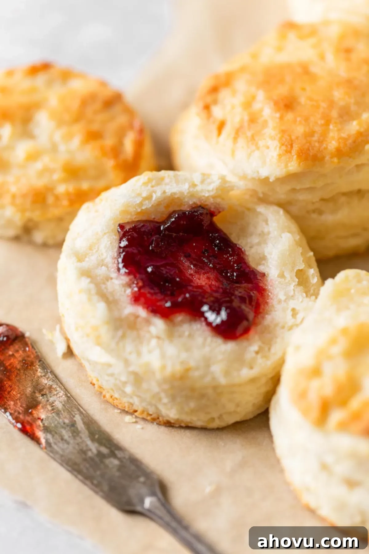 A homemade buttermilk biscuit split in half and topped with jam. More biscuits surround it. 