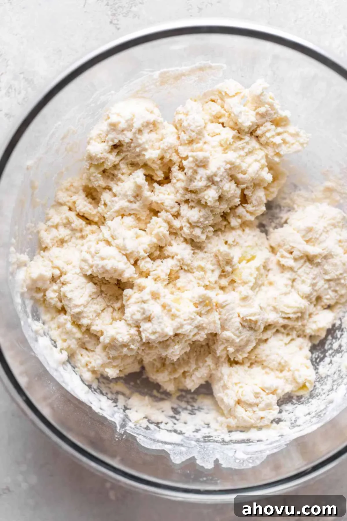 Overhead view of raw biscuit dough in a glass mixing bowl. 