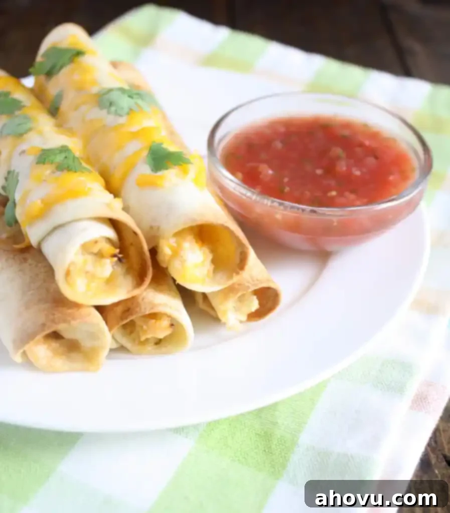Five baked chicken taquitos on a white plate with a dish of salsa. 