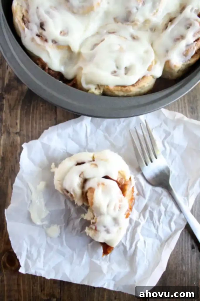 Overhead view of 1 hour cinnamon rolls in a round pan. A half-eaten cinnamon roll and a fork rest nearby on a piece of paper. 