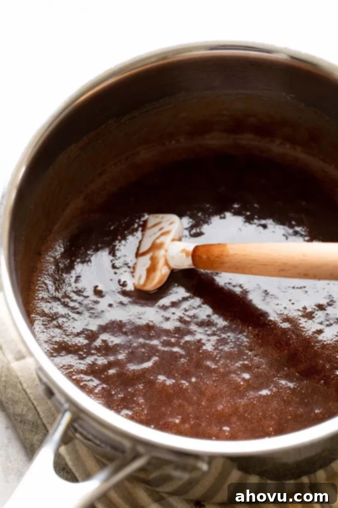 The foundational mixture for no-bake cookies—butter, sugar, milk, and cocoa powder—simmering in a large saucepan after being melted and boiled for one minute, with a rubber spatula resting inside.