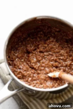 The fully mixed no-bake cookie batter after quick-cooking oats have been thoroughly incorporated, appearing thick and cohesive in a saucepan.