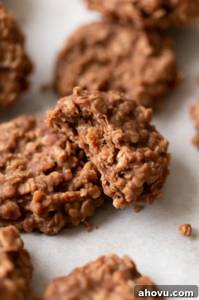 Several perfectly set no-bake cookies displayed on parchment paper, with one cookie showing a delicious bite taken out of it, revealing its chewy interior of oats, peanut butter, and chocolate.
