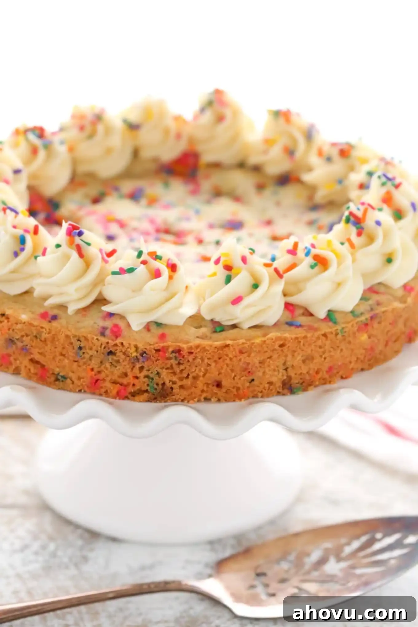 A sugar cookie cake topped with whirls of vanilla buttercream, seen from the side. 