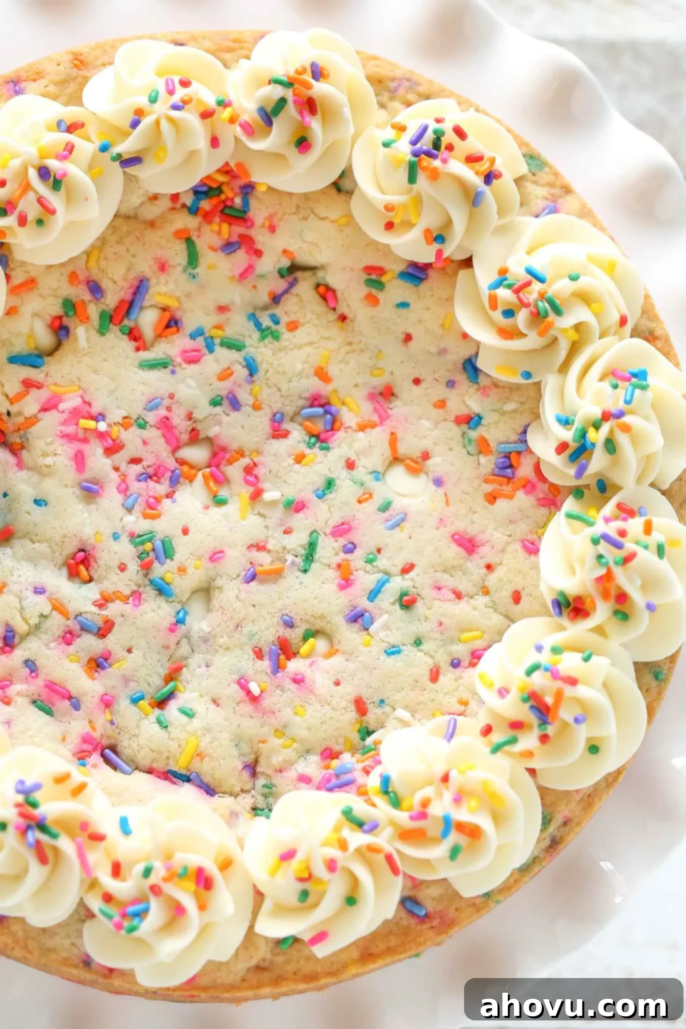 Overhead view of a birthday cookie cake topped with sprinkles and vanilla frosting. 
