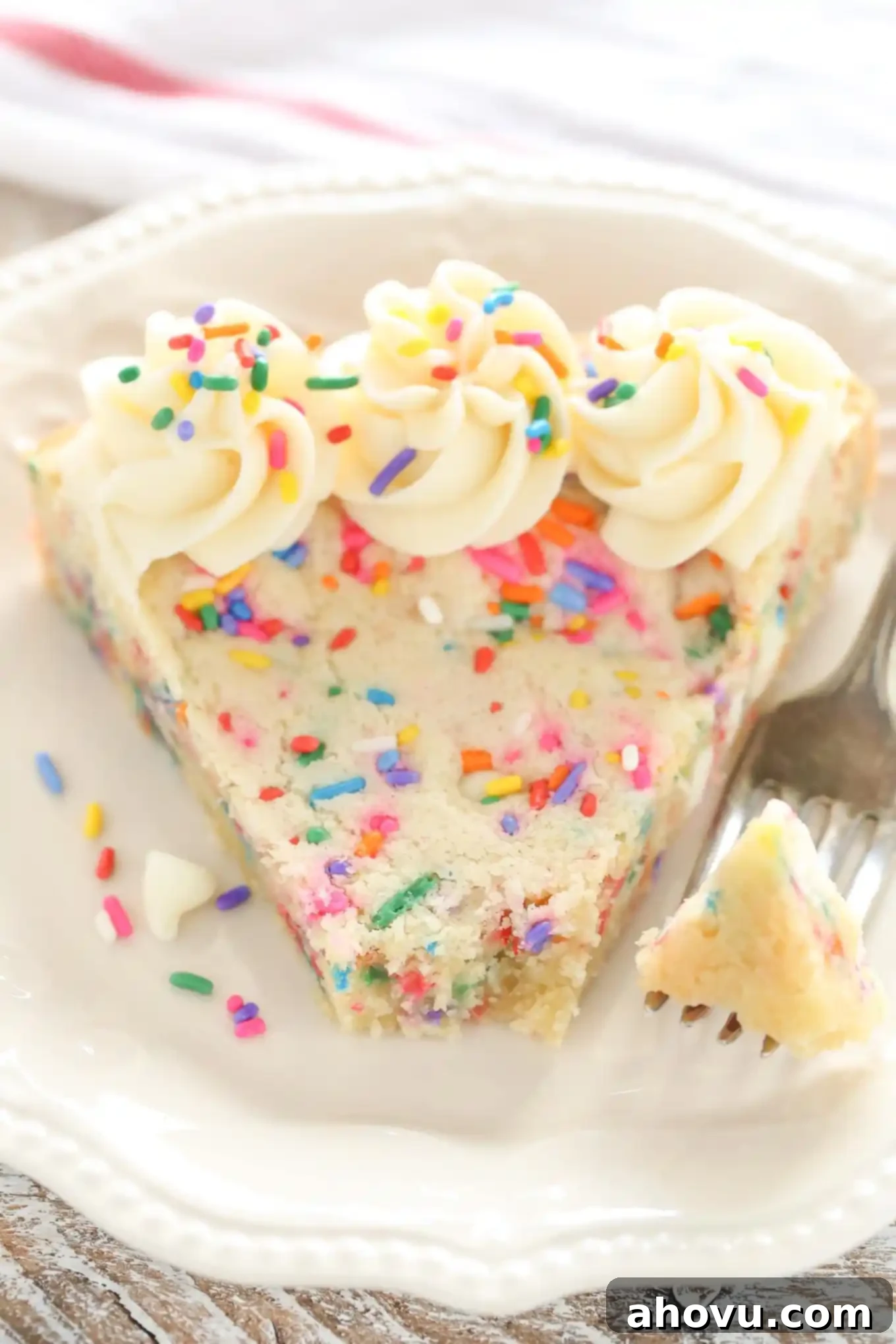 A slice of funfetti sugar cookie cake on a white plate with a fork. The fork has speared a bite of the cake. 