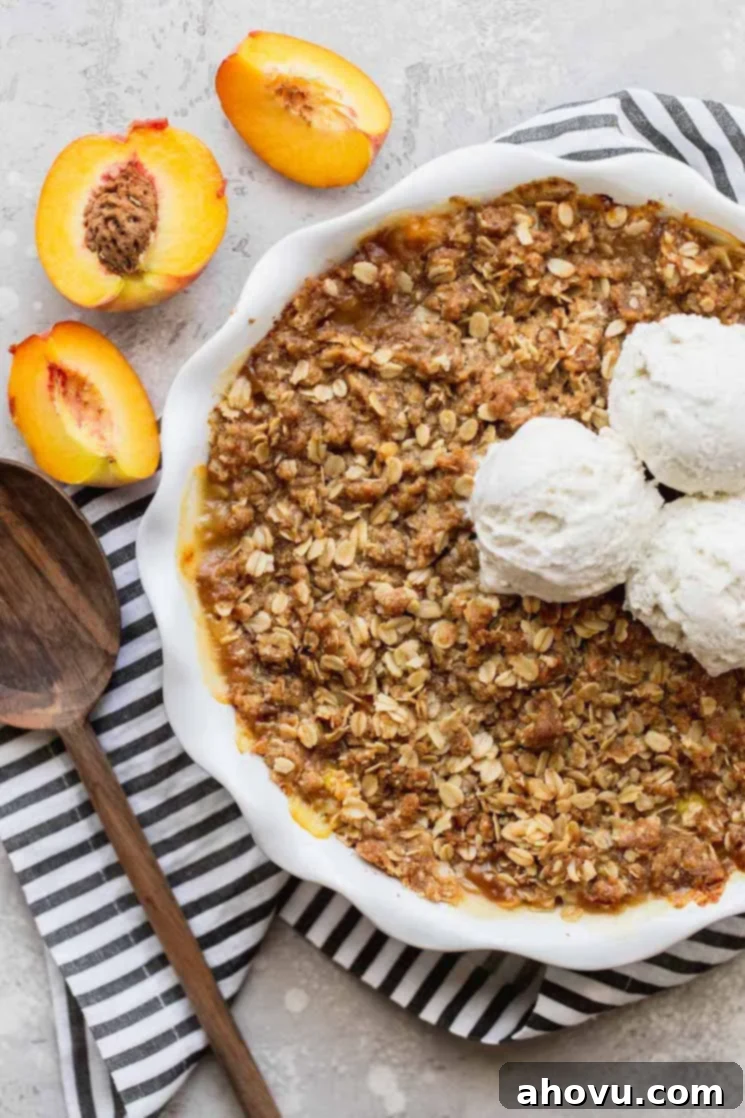 Golden Peach Crumble 2 A finished peach crisp in a white baking dish topped with a scoop of vanilla ice cream, with a sliced peach half resting beside it.