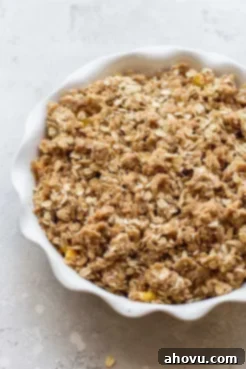 A round white baking dish filled with sliced peaches, evenly covered with the oat crisp topping, ready for baking.