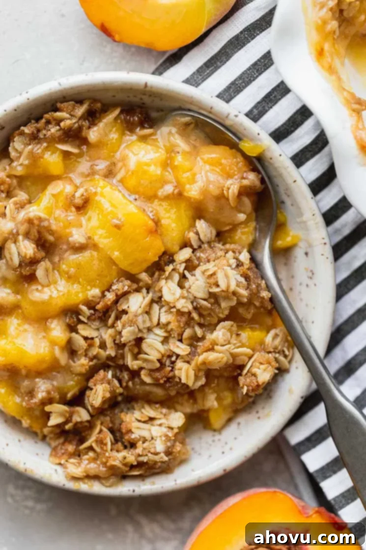 Golden Peach Crumble 5 A single serving of peach crisp in a white bowl with a spoon, showing the juicy peaches and crispy topping.