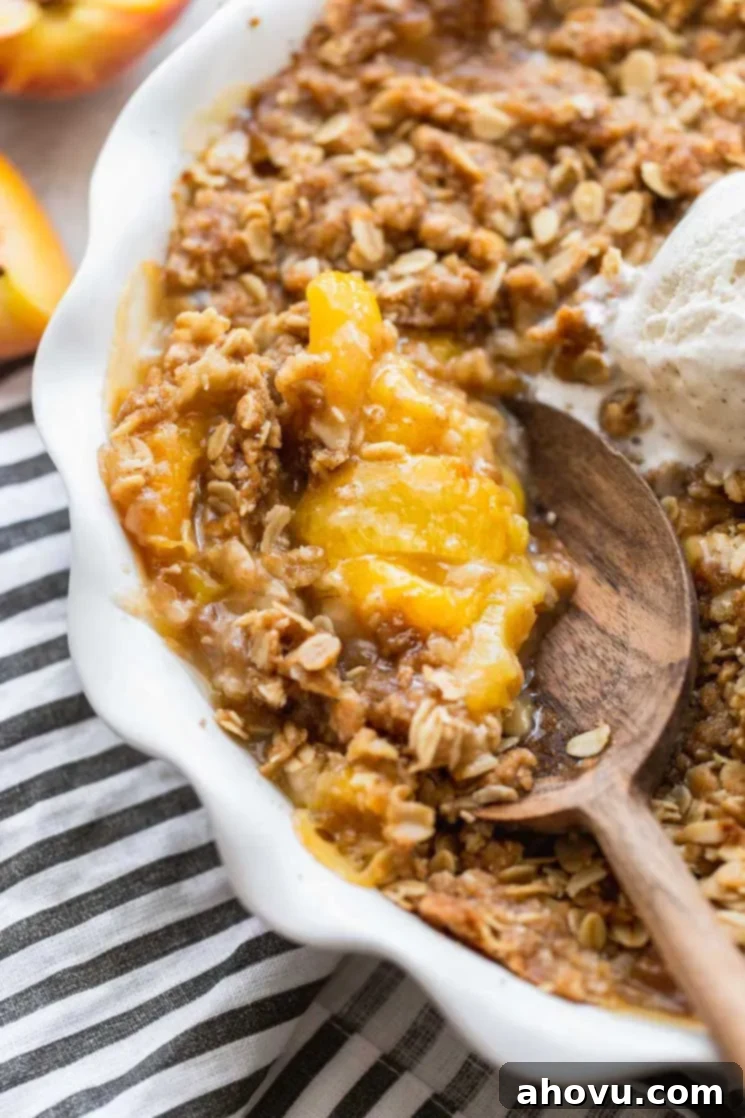 Golden Peach Crumble 6 A finished peach crisp in a round baking dish being scooped with a wooden spoon, showcasing the bubbling fruit and crispy topping.