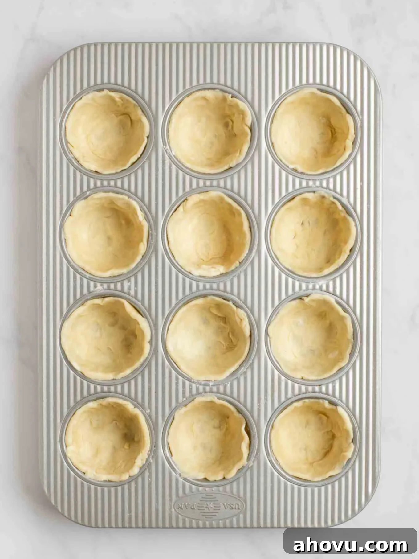 An overhead view of pie crust circles pressed into the cavities of a muffin pan.