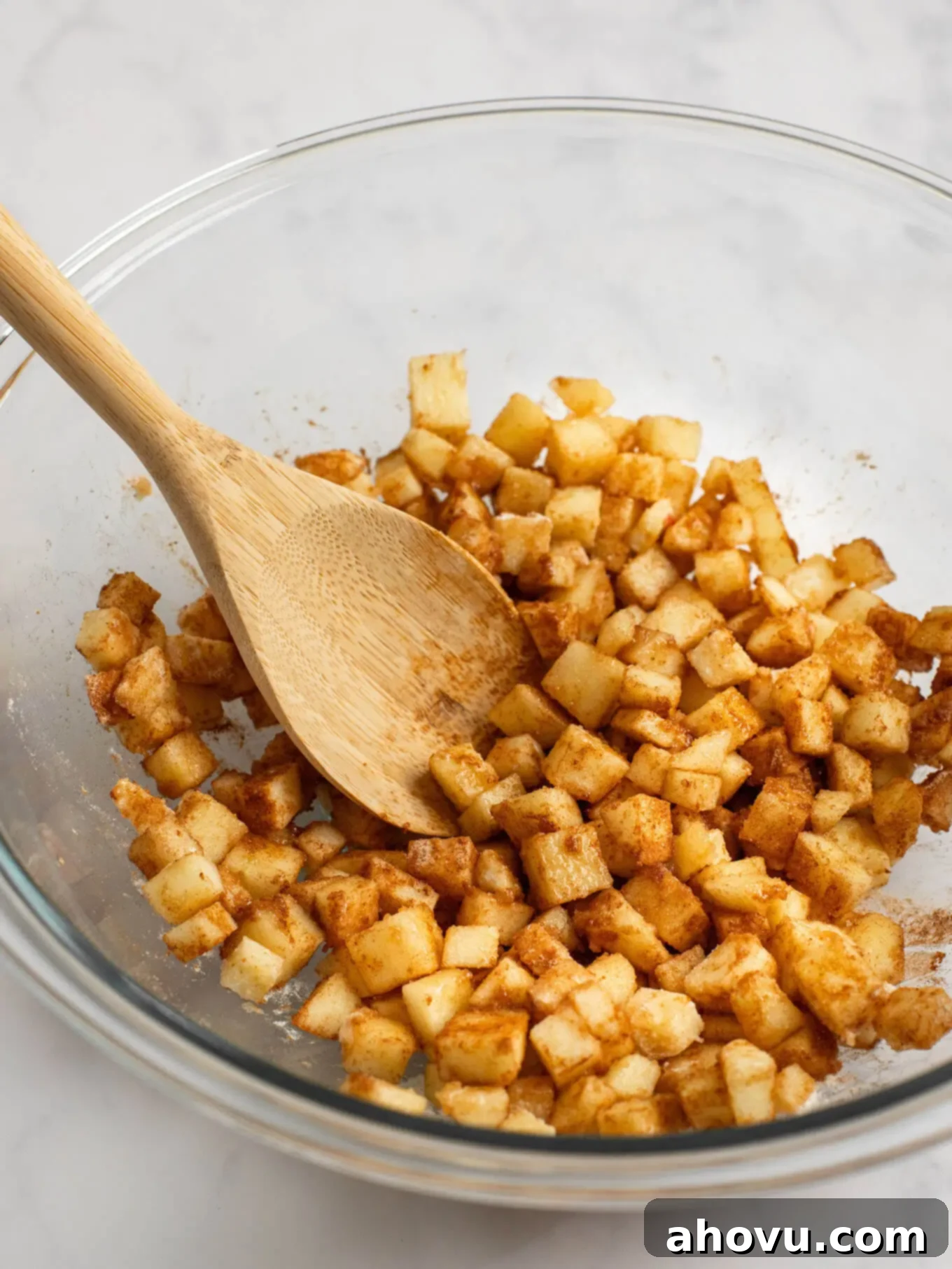 Apple pie filling mixed together in a glass mixing bowl with a wooden spoon.