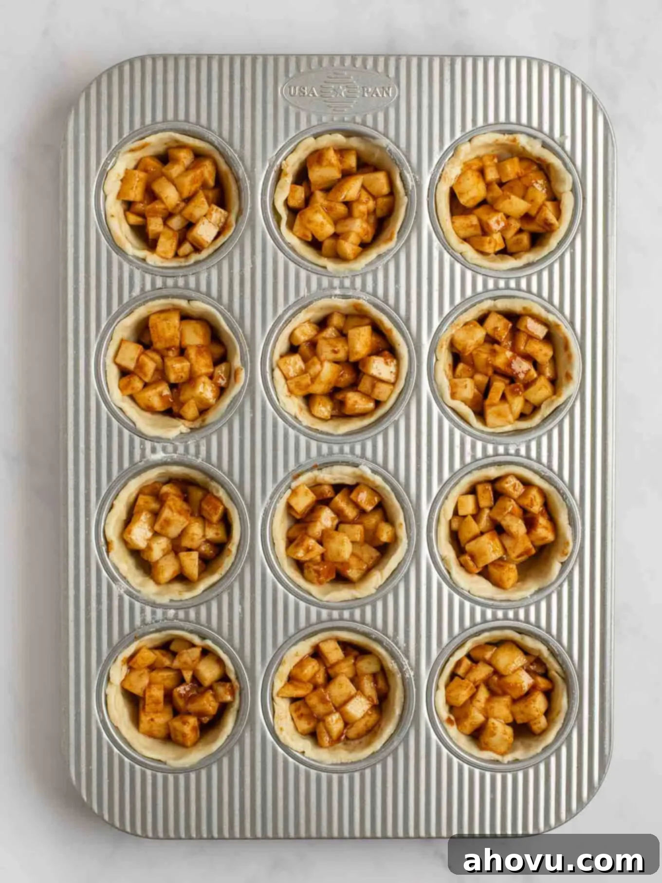 An overhead view of the apple pie filling evenly distributed between all of the pie crusts in a muffin pan.