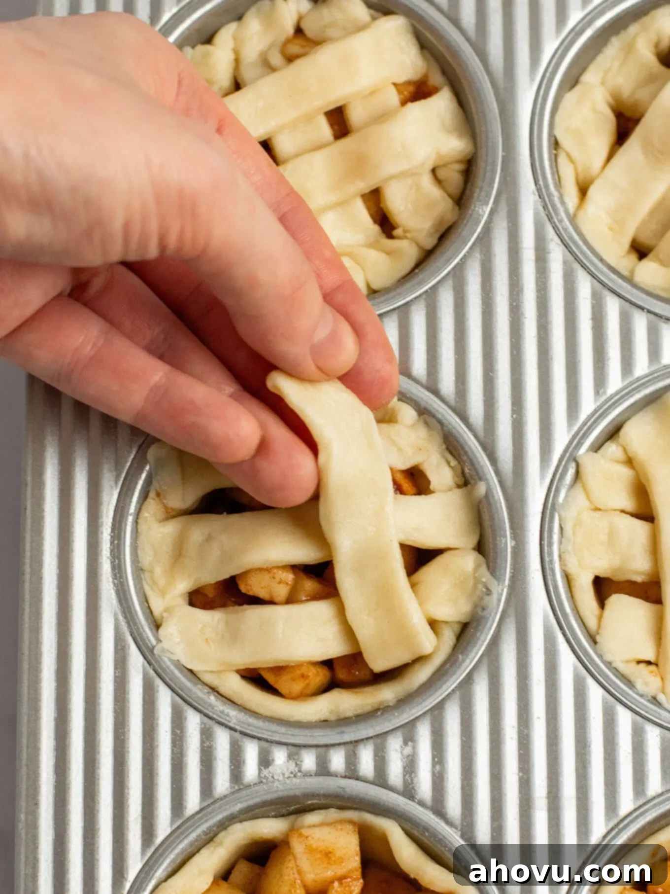 An angled view of small strips of pie crust being placed on top of the pies to create a lattice pie crust.