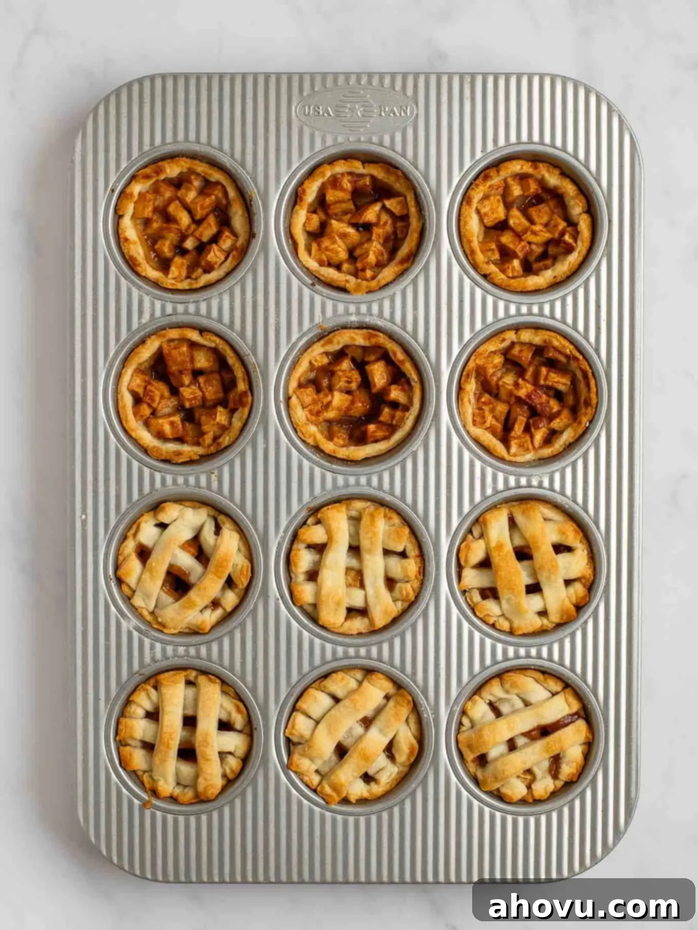 An overhead view of the baked mini apple pies in a muffin pan. Half of the mini pies have a lattice pie crust topping.