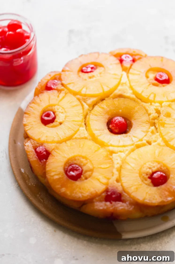 Golden Pineapple Flip Cake 2 A finished pineapple upside down cake resting on a plate with a jar of cherries in the background.