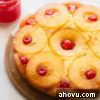 Golden Pineapple Flip Cake 7 A whole pineapple upside down cake on a plate with a jar of cherries in the background.