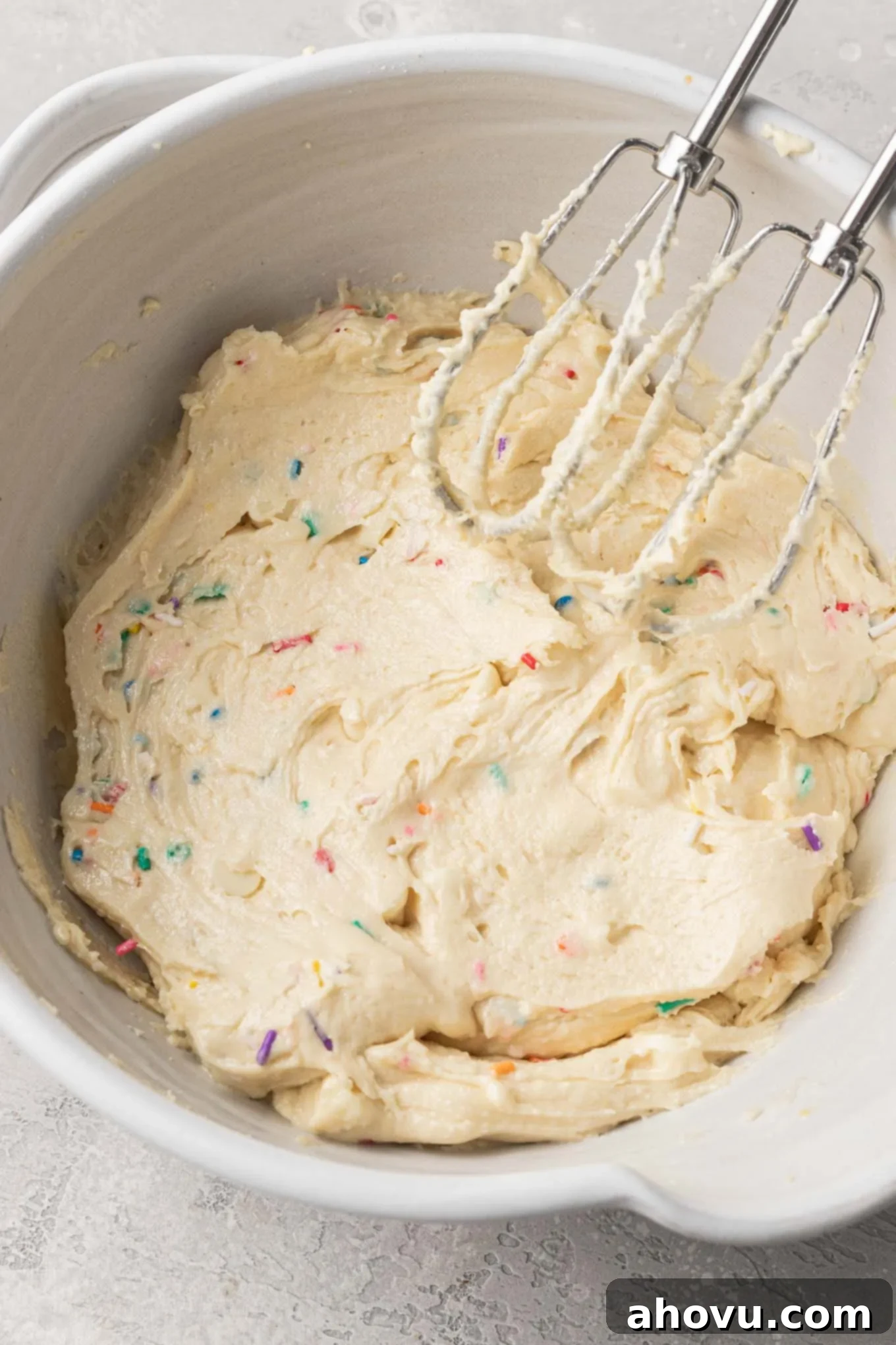 Cookie dough in a mixing bowl, with electric beaters resting on the side. A close-up view of freshly mixed cookie dough in a large bowl, with electric beaters resting nearby, indicating it's ready for the next step.