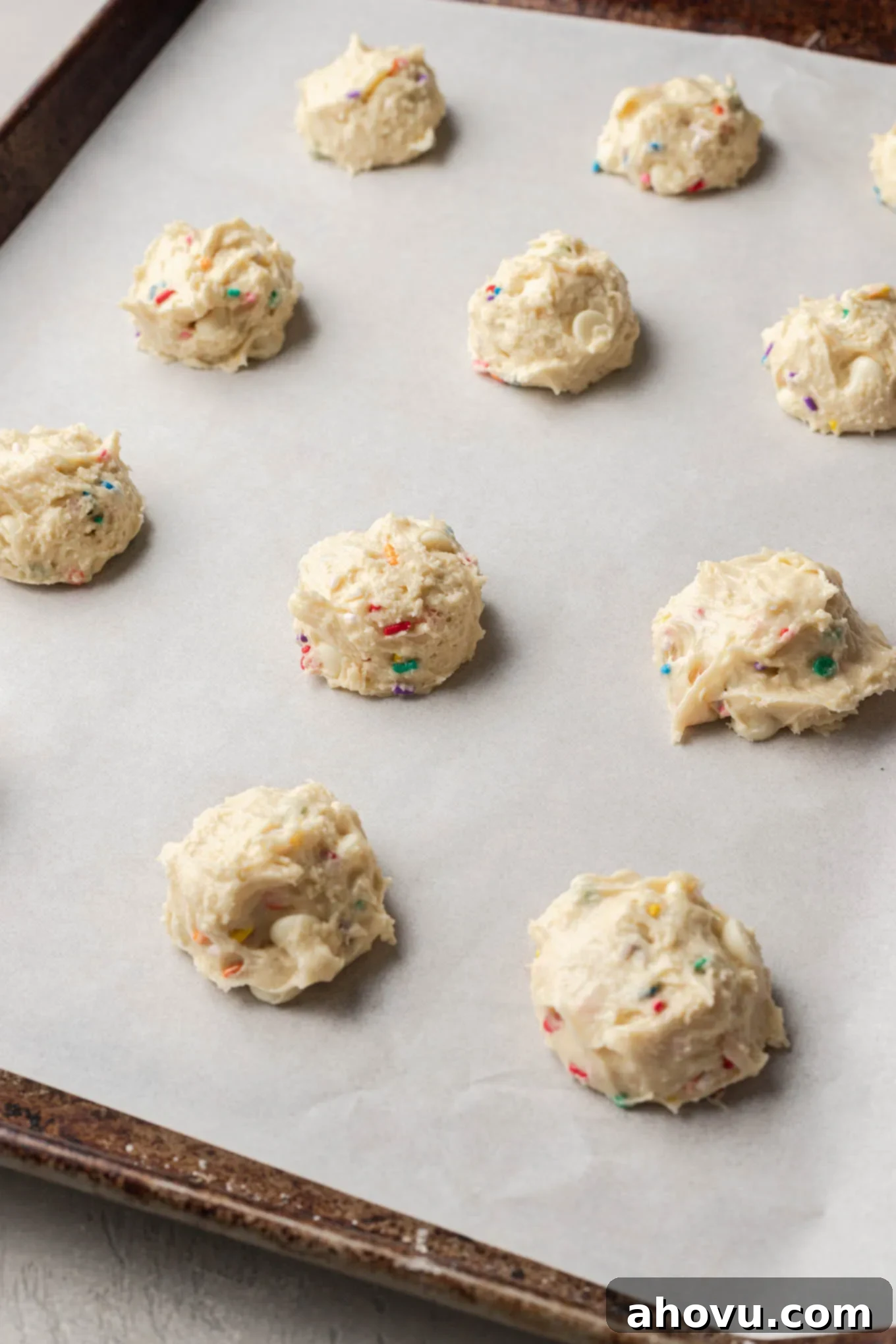 Cookie dough balls on a parchment paper-lined baking sheet. Perfectly portioned cookie dough balls, evenly spaced on a baking sheet lined with parchment paper, awaiting their transformation in the oven.