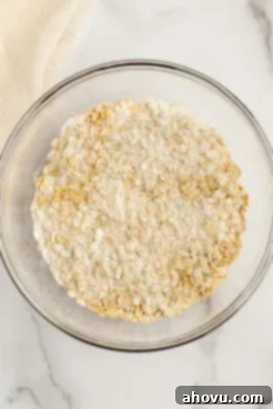 A glass bowl with the dry ingredients mixed together for monster cookies, featuring flour, oats, baking soda, and salt.