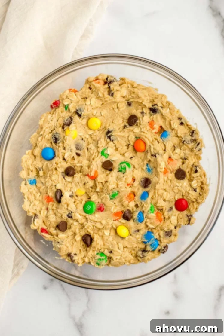 A glass bowl filled with monster cookie dough on top of a marble surface, ready for scooping and baking.