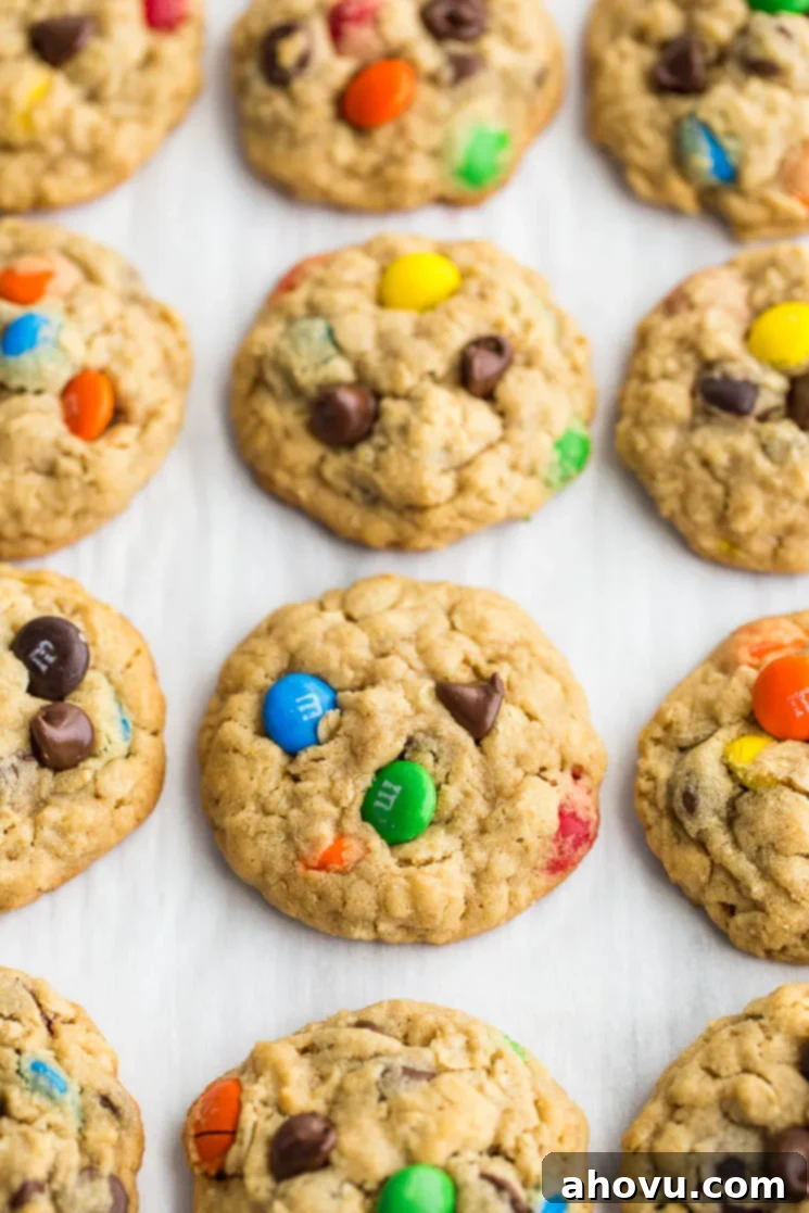 Baked monster cookies lined up on a piece of parchment paper, showing their perfectly golden edges and colorful M&M's.