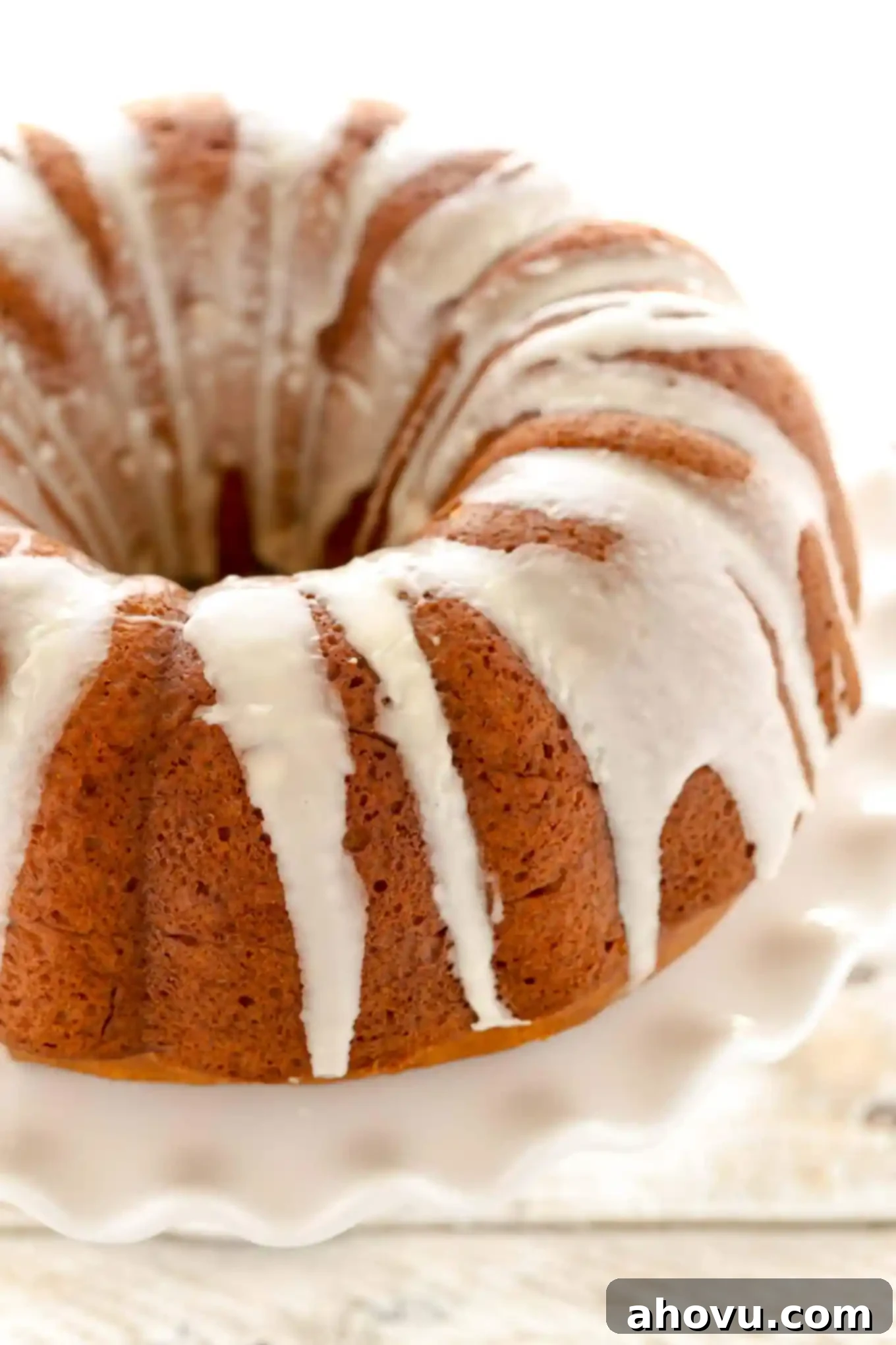 Pumpkin Swirl Cream Cheese Bundt 2 A beautifully baked homemade pumpkin bundt cake filled with cream cheese and drizzled with a sweet vanilla glaze, presented on a stand.