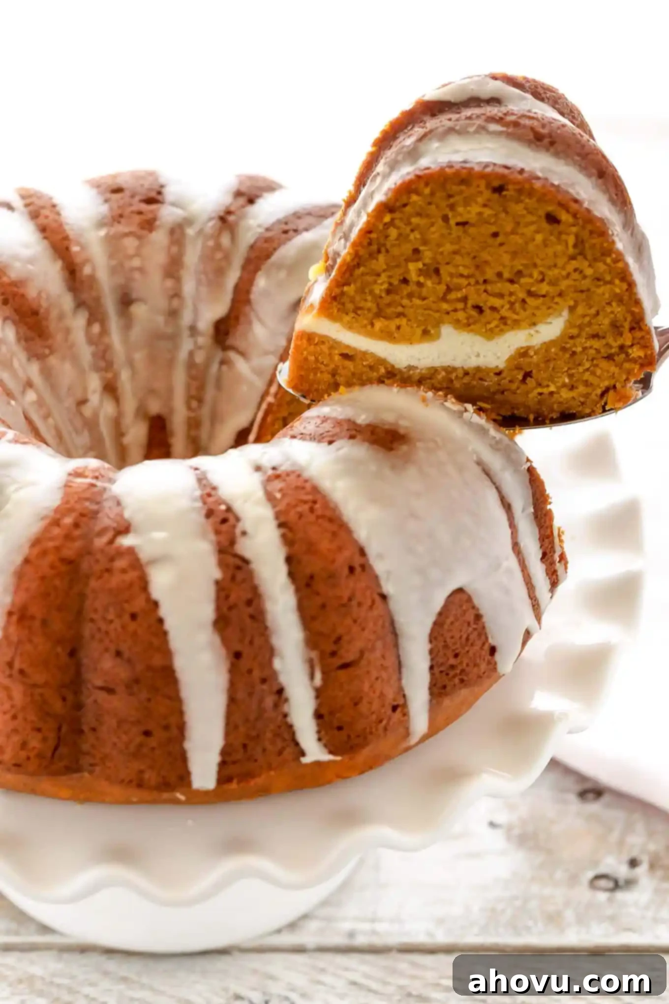 Pumpkin Swirl Cream Cheese Bundt 3 A perfect slice of pumpkin spice bundt cake, revealing the cream cheese swirl, being carefully removed from a cake stand.
