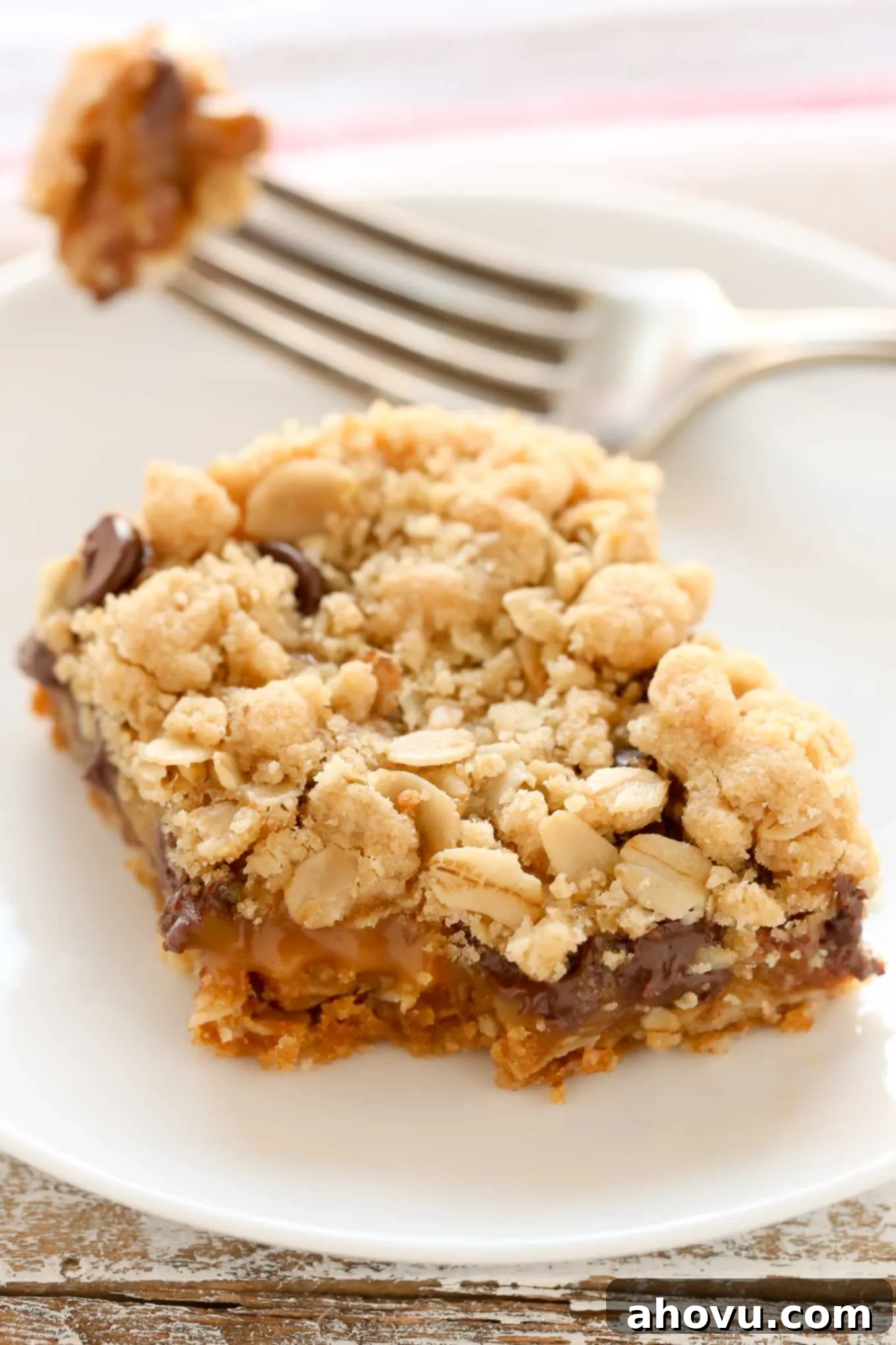 The Carmelitas 4 An oatmeal carmelita slice on a white plate. A fork rests on the plate.