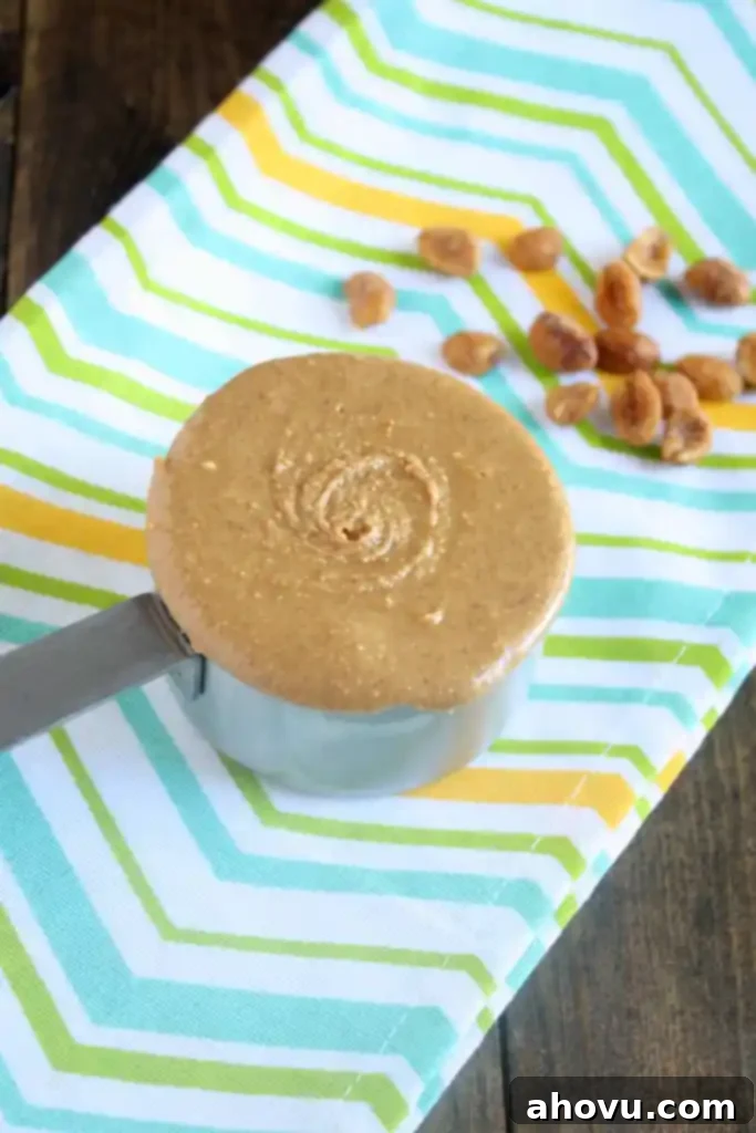 A measuring cup of honey peanut butter on a striped towel. 