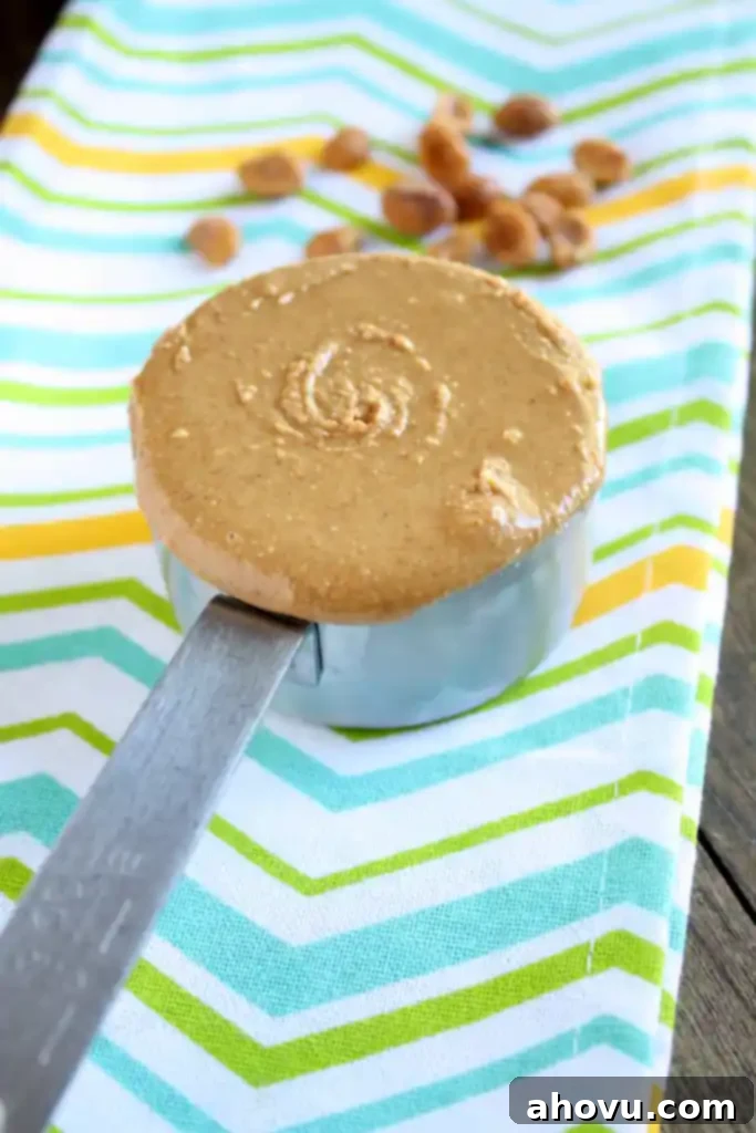A measuring cup of honey peanut butter on a striped towel. 