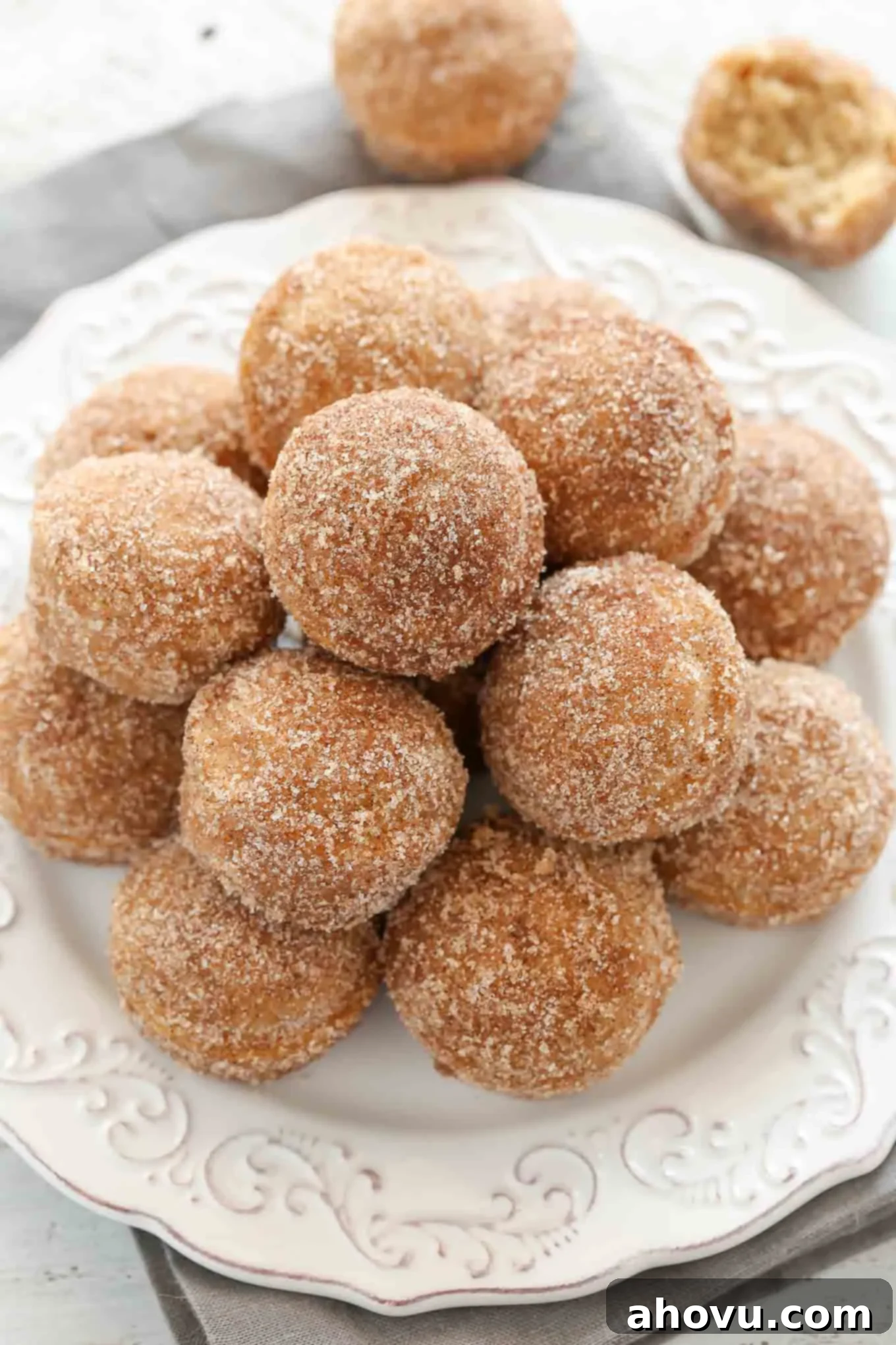Oven-Fresh Apple Cider Donut Bites 4 An inviting overhead view of a pristine white plate, generously piled high with golden-brown apple cinnamon donut holes, dusted with a sparkling sugar coating.