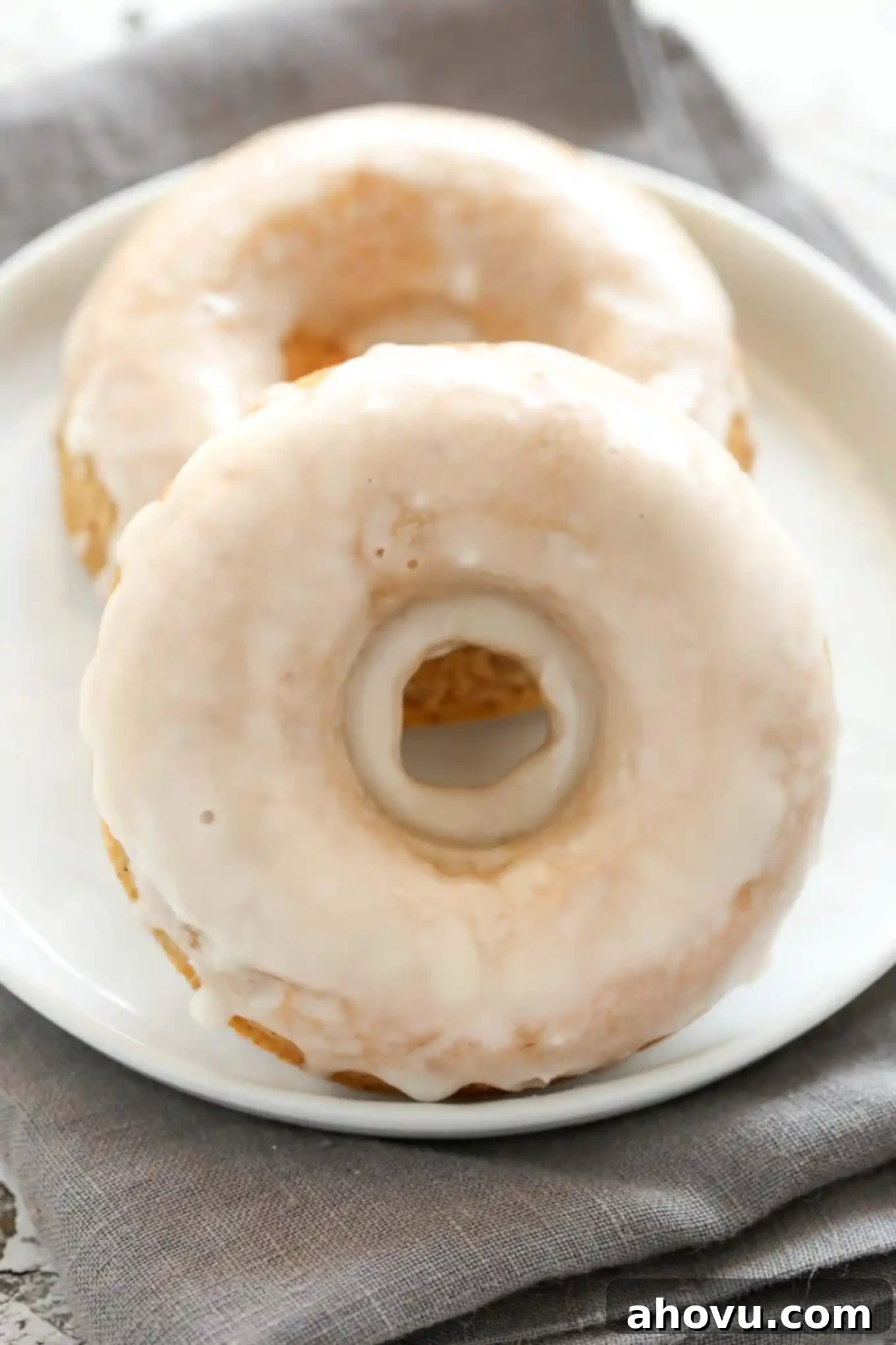 Oven-Fresh Apple Cider Donut Bites 5 A simple yet elegant shot of two perfectly glazed baked apple cider donuts resting on a white plate, showcasing their smooth, glistening finish.