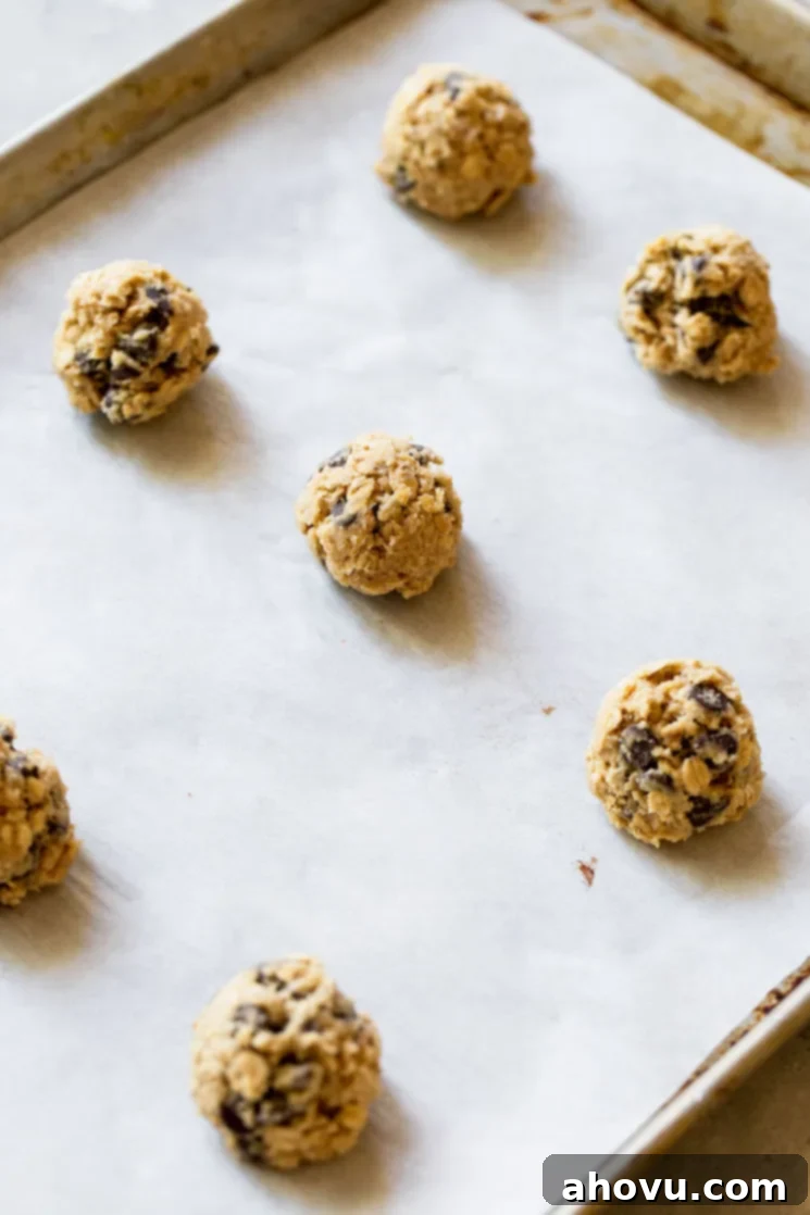 An antique baking sheet beautifully lined with parchment paper, holding evenly spaced balls of oatmeal chocolate chip cookie dough, perfectly prepped and ready for baking.