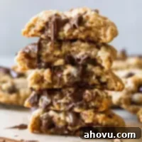 A stack of soft and chewy oatmeal chocolate chip cookies, one cut in half revealing its interior, with melted chocolate cascading down, highlighting their rich flavor and perfect texture.