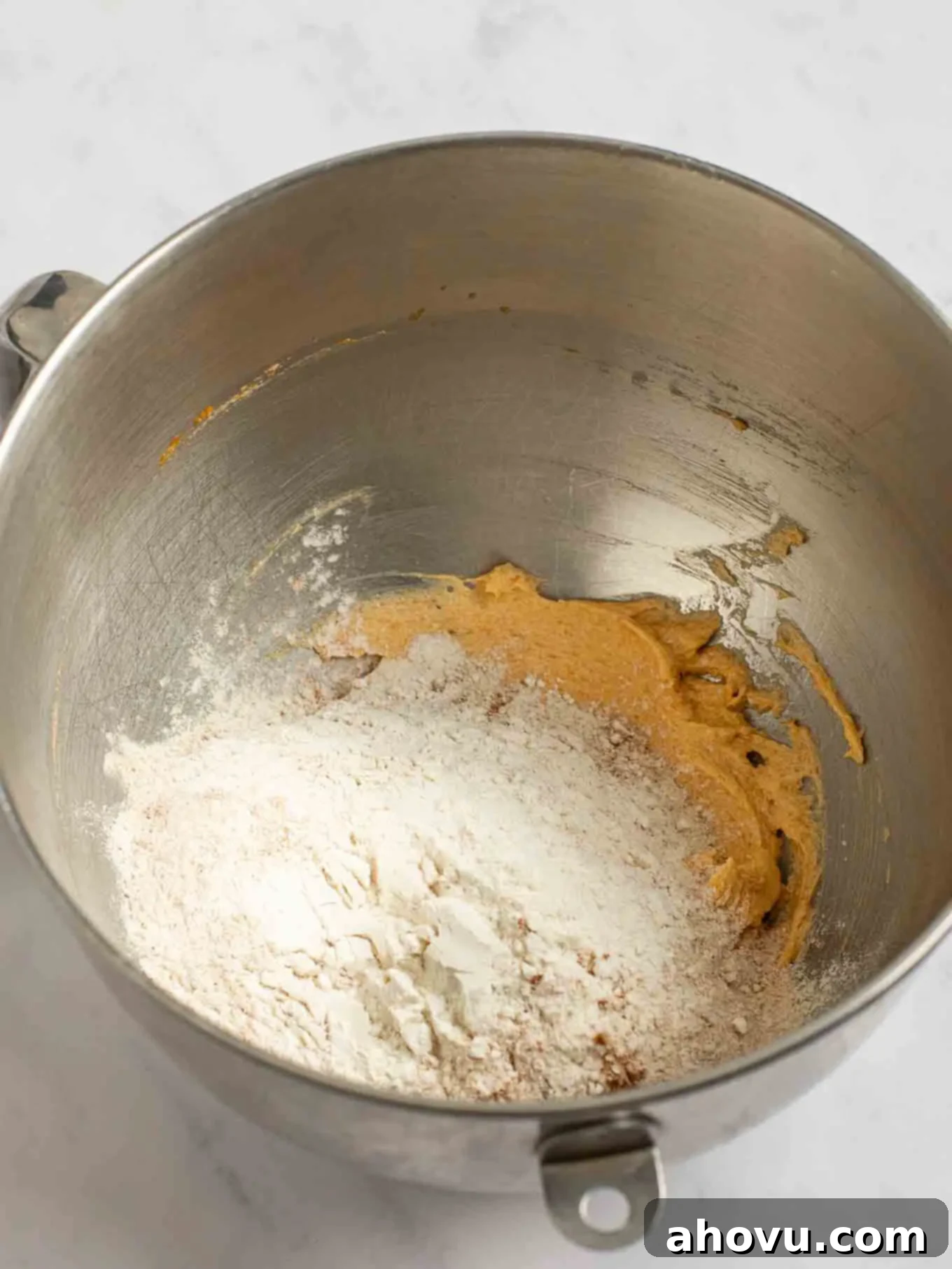 Spiced Pumpkin Snickerdoodles 6 The pre-whisked dry ingredients, a mixture of flour and spices, carefully added on top of the creamy wet ingredients within the bowl of a stand mixer, ready for gentle combining.