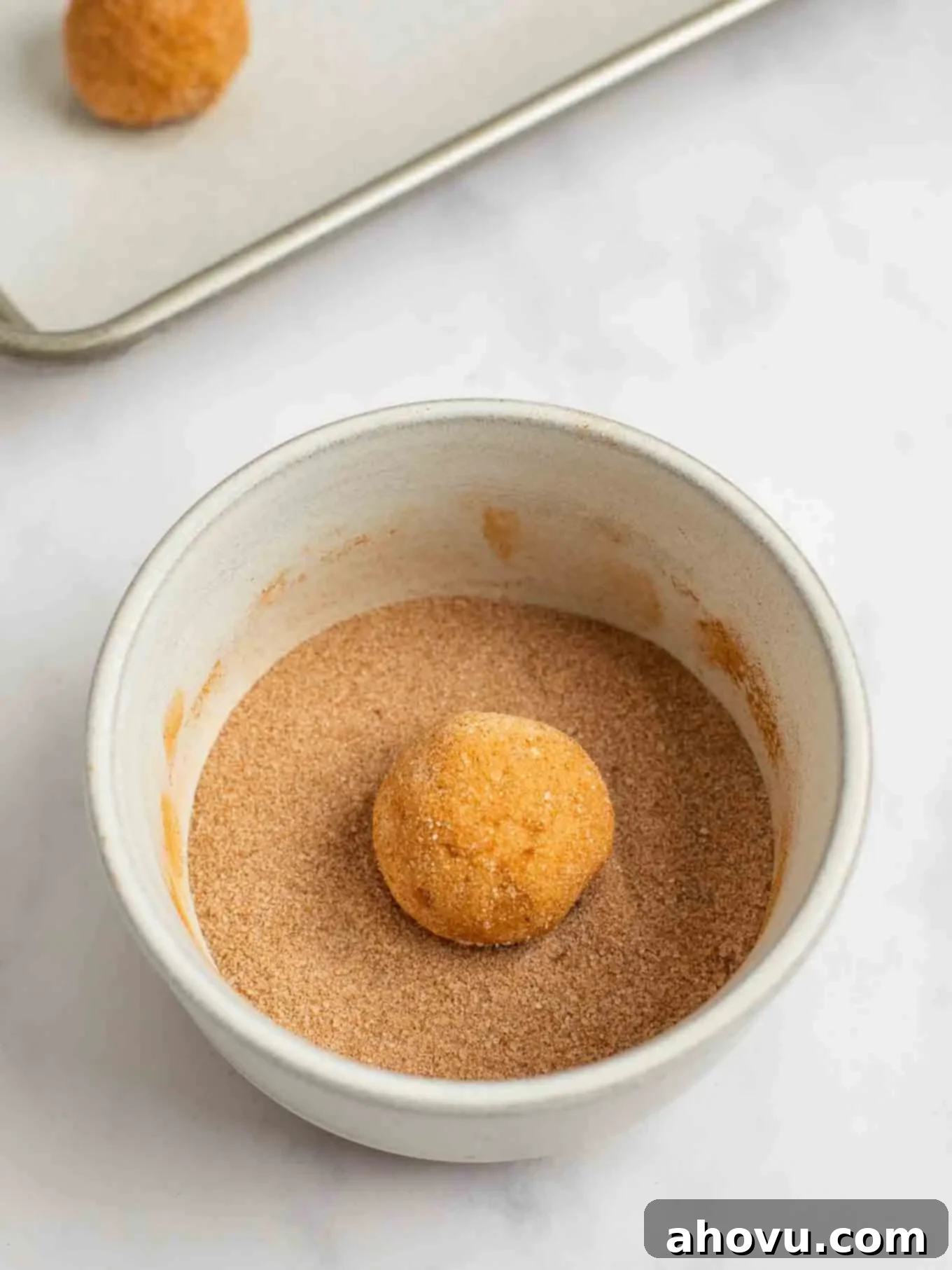 Spiced Pumpkin Snickerdoodles 8 A perfectly portioned ball of pumpkin snickerdoodle cookie dough being gently rolled in a fragrant mixture of cinnamon and sugar, ready for baking.