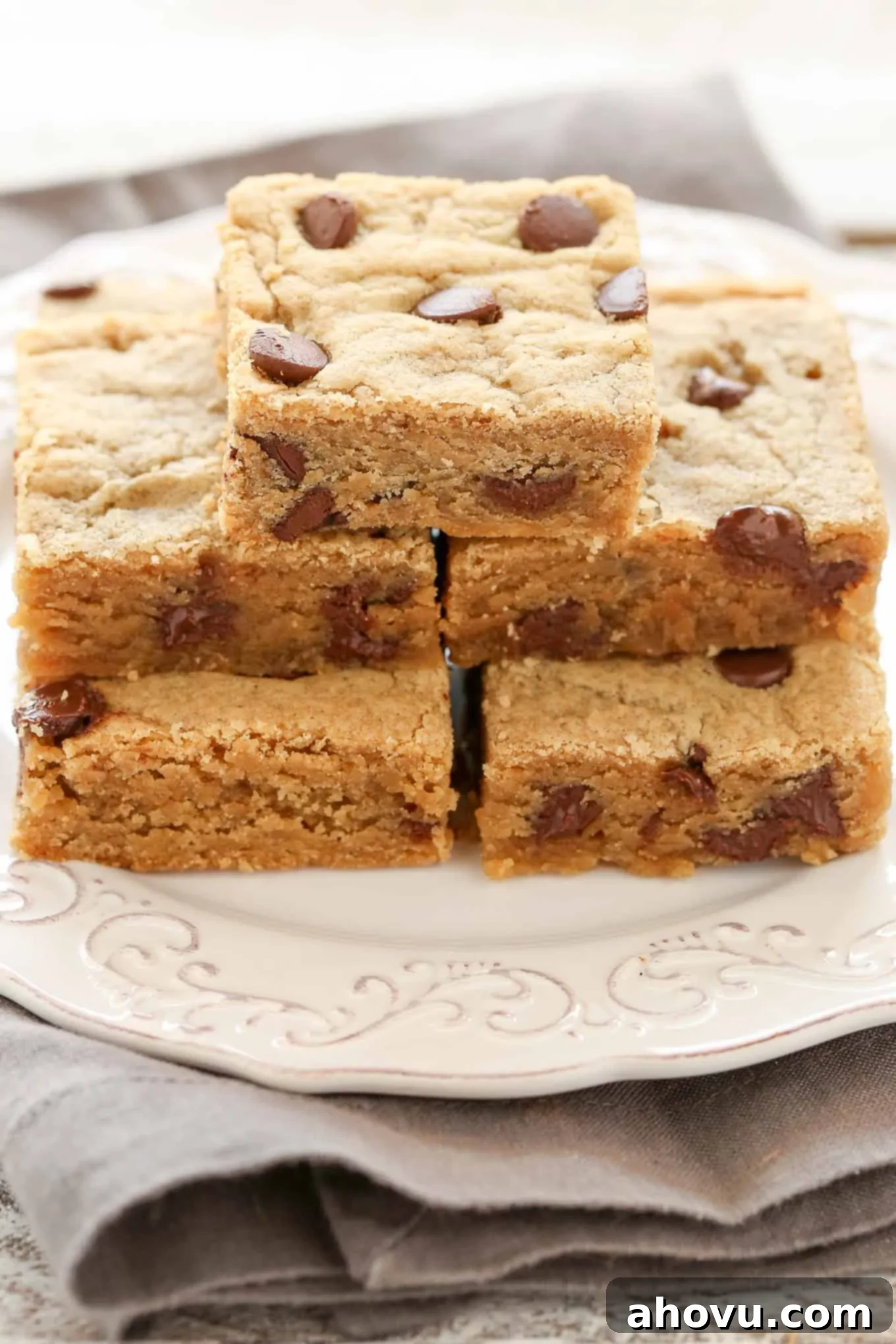Five peanut butter chocolate chip bars stacked on a white plate. 