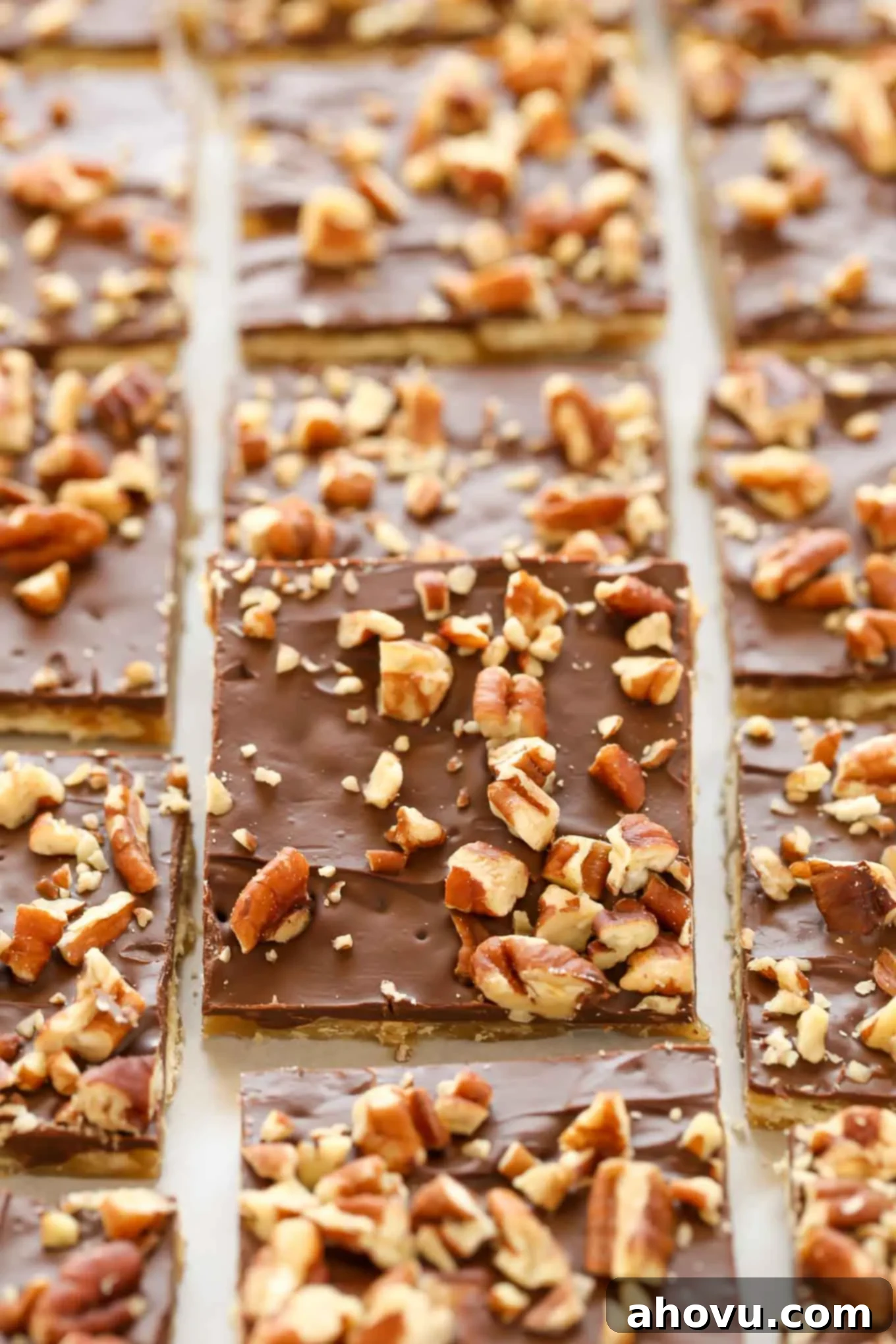 Golden saltine toffee squares topped with melted chocolate and chopped pecans on a parchment-lined baking sheet, ready for chilling.