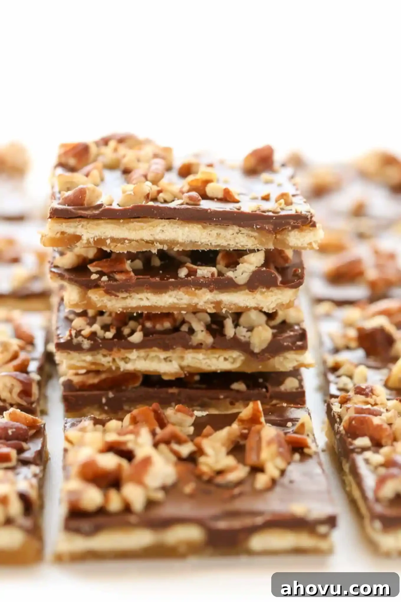 A close-up of Saltine Toffee broken into irregular pieces, showcasing the cracker base, golden toffee, and melted chocolate with pecan topping.