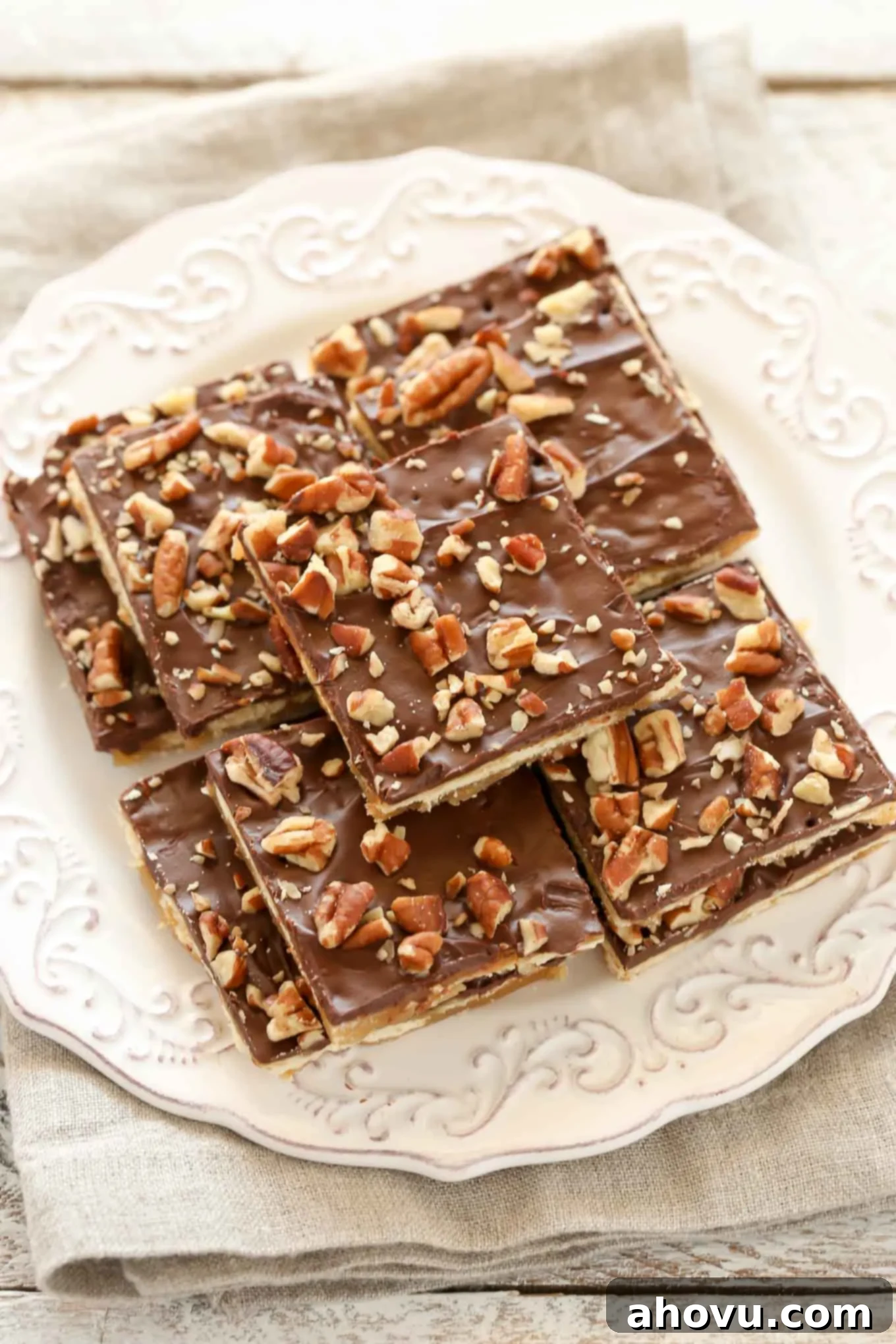 Saltine Toffee squares neatly arranged on a white plate, showcasing the chocolate and pecan topping.