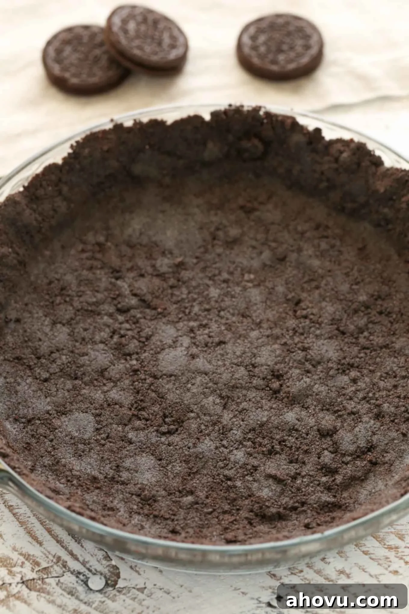 An Oreo pie crust in a glass pie plate. Three Oreos rest in the background. 