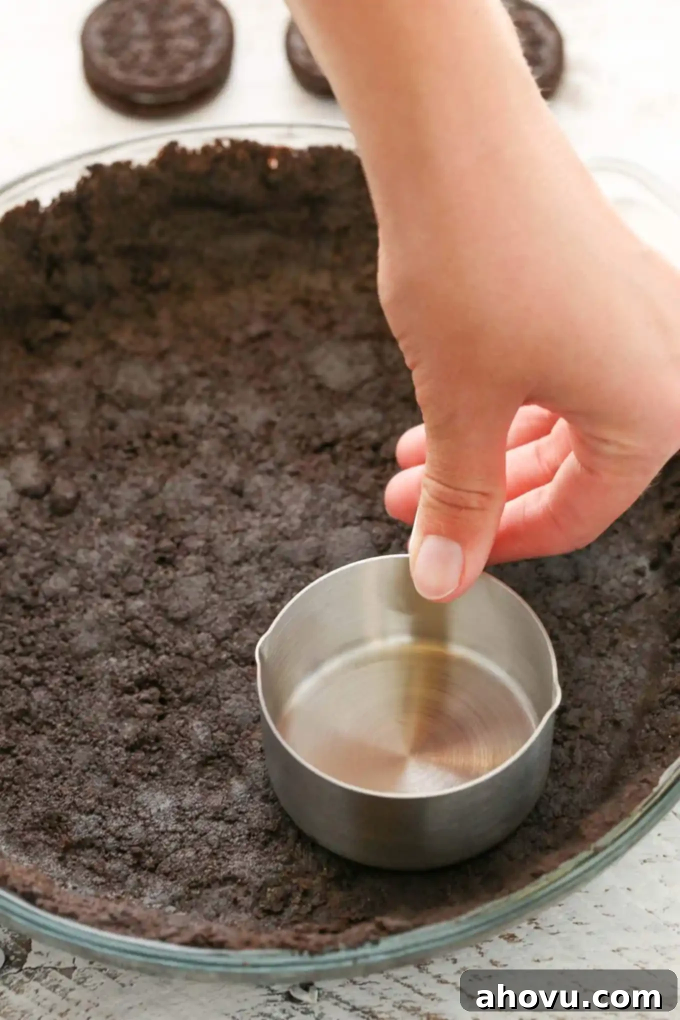 Process shot showing a measuring cup being used to pack down an Oreo cookie pie crust. 