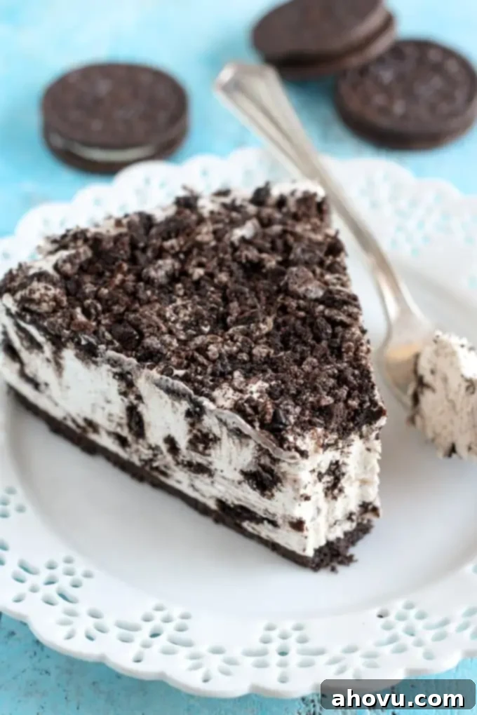 A slice of no-bake Oreo cheesecake on a white plate. Three Oreos rest in the background. 
