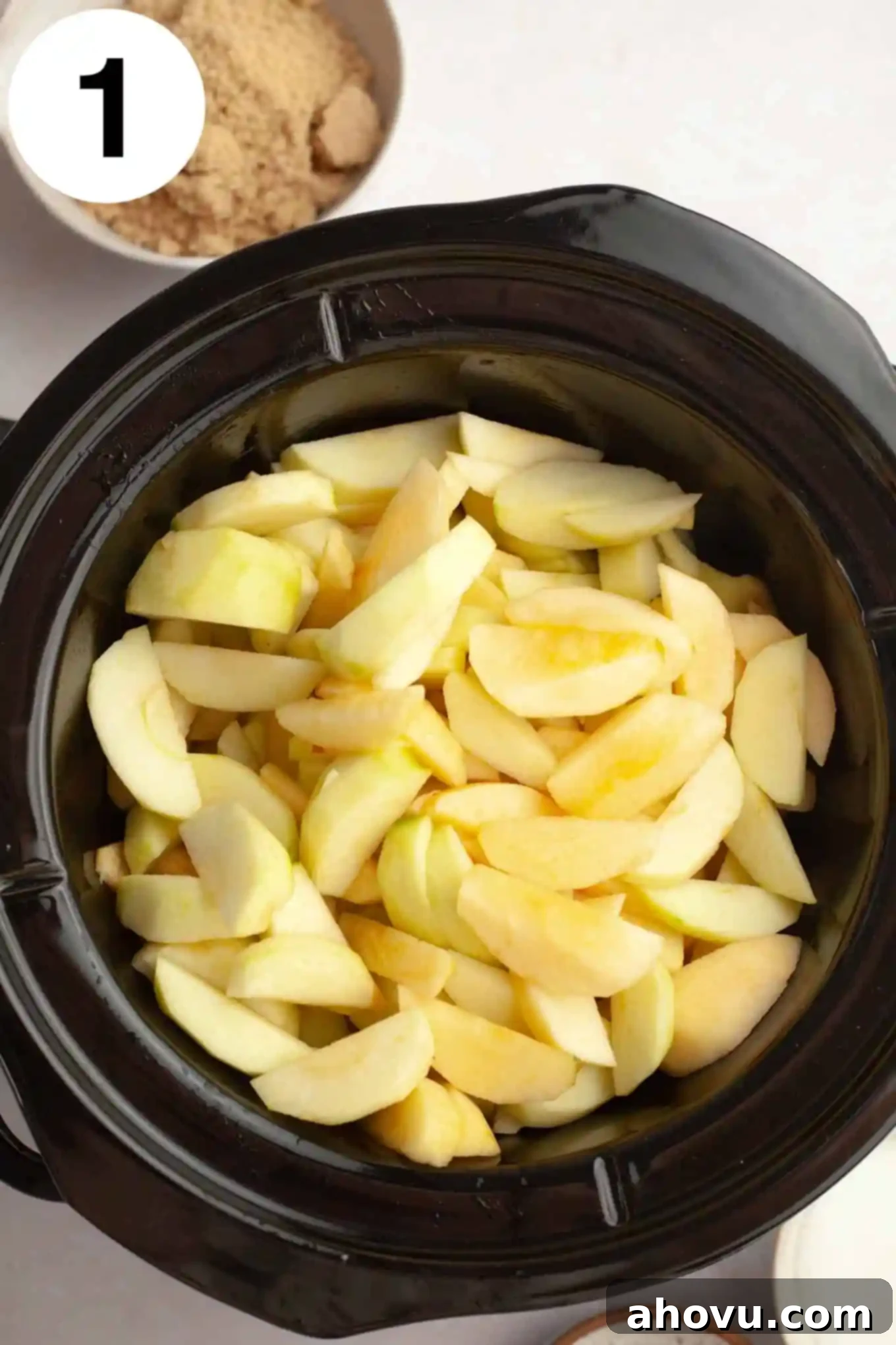 Homemade Spiced Apple Butter 4 Sliced apples, peeled and cored, are neatly arranged inside a slow cooker, ready for the next steps of making slow cooker apple butter.