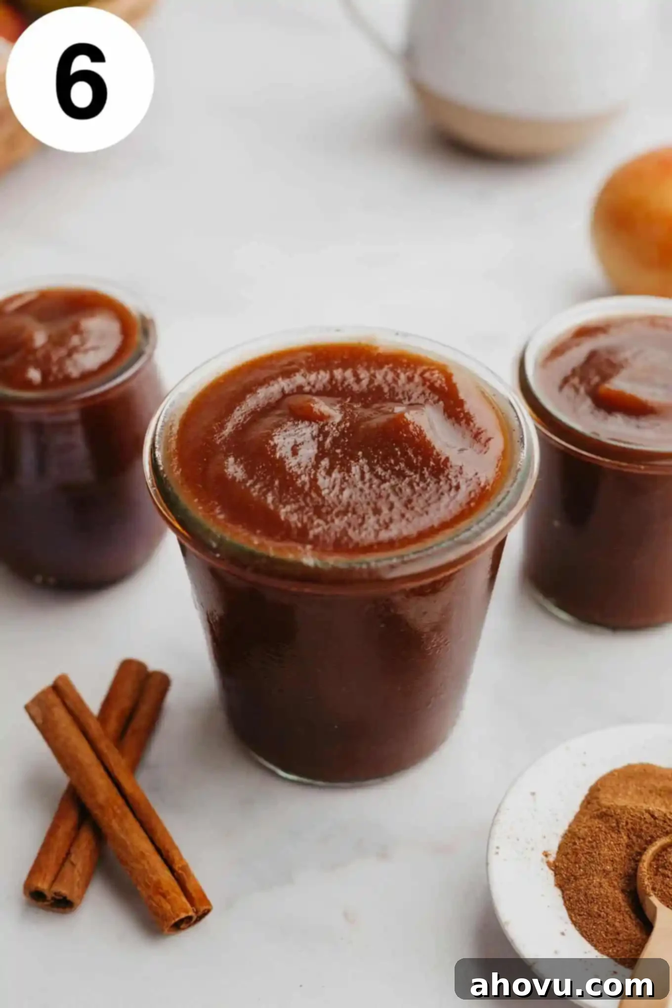 Homemade Spiced Apple Butter 9 Three glass jars of freshly made apple butter, beautifully displayed on a counter with scattered cinnamon sticks, star anise, and whole cloves, evoking a warm, inviting fall scene.
