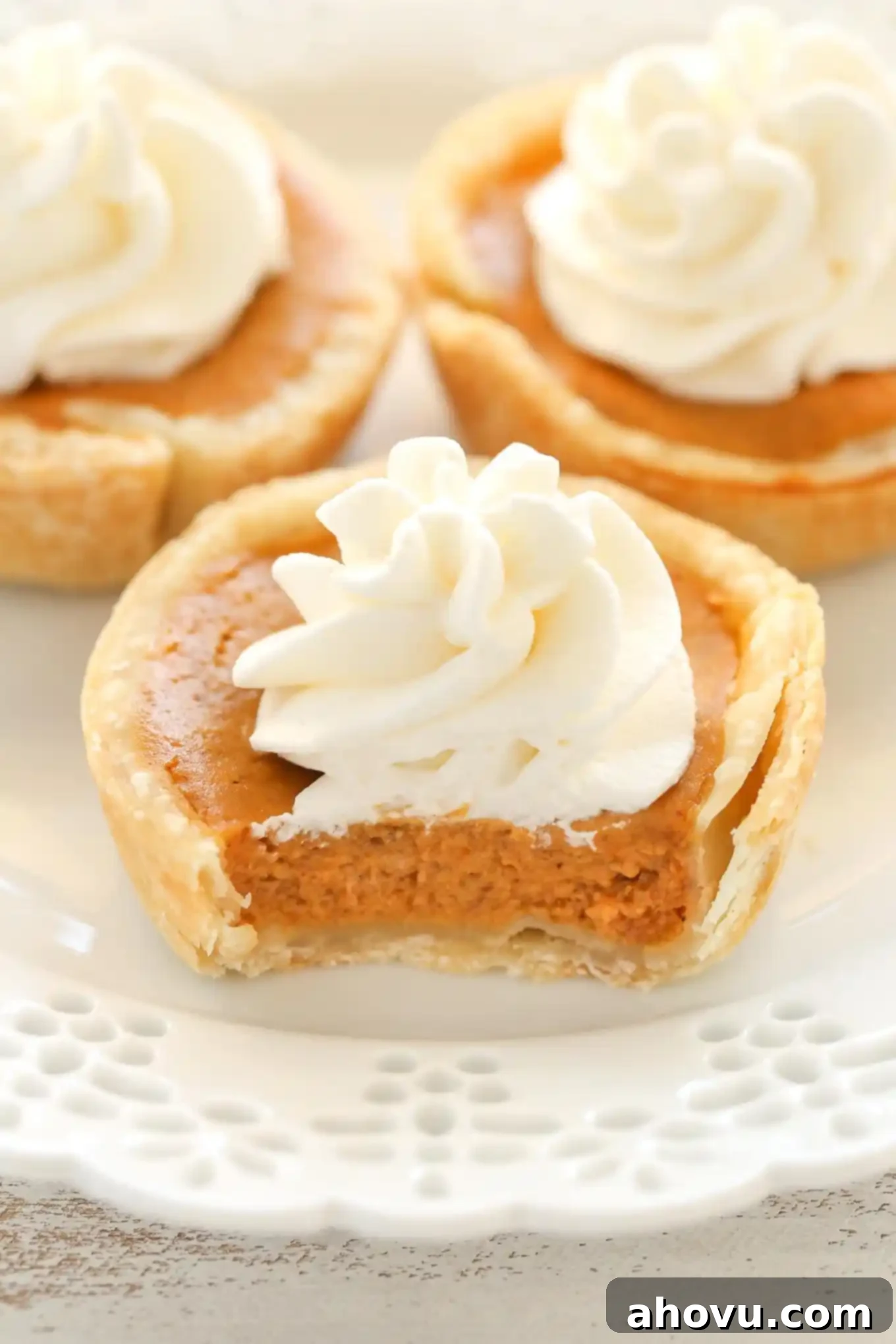 Three mini pumpkin pies topped with whipped cream on a decorative white plate.