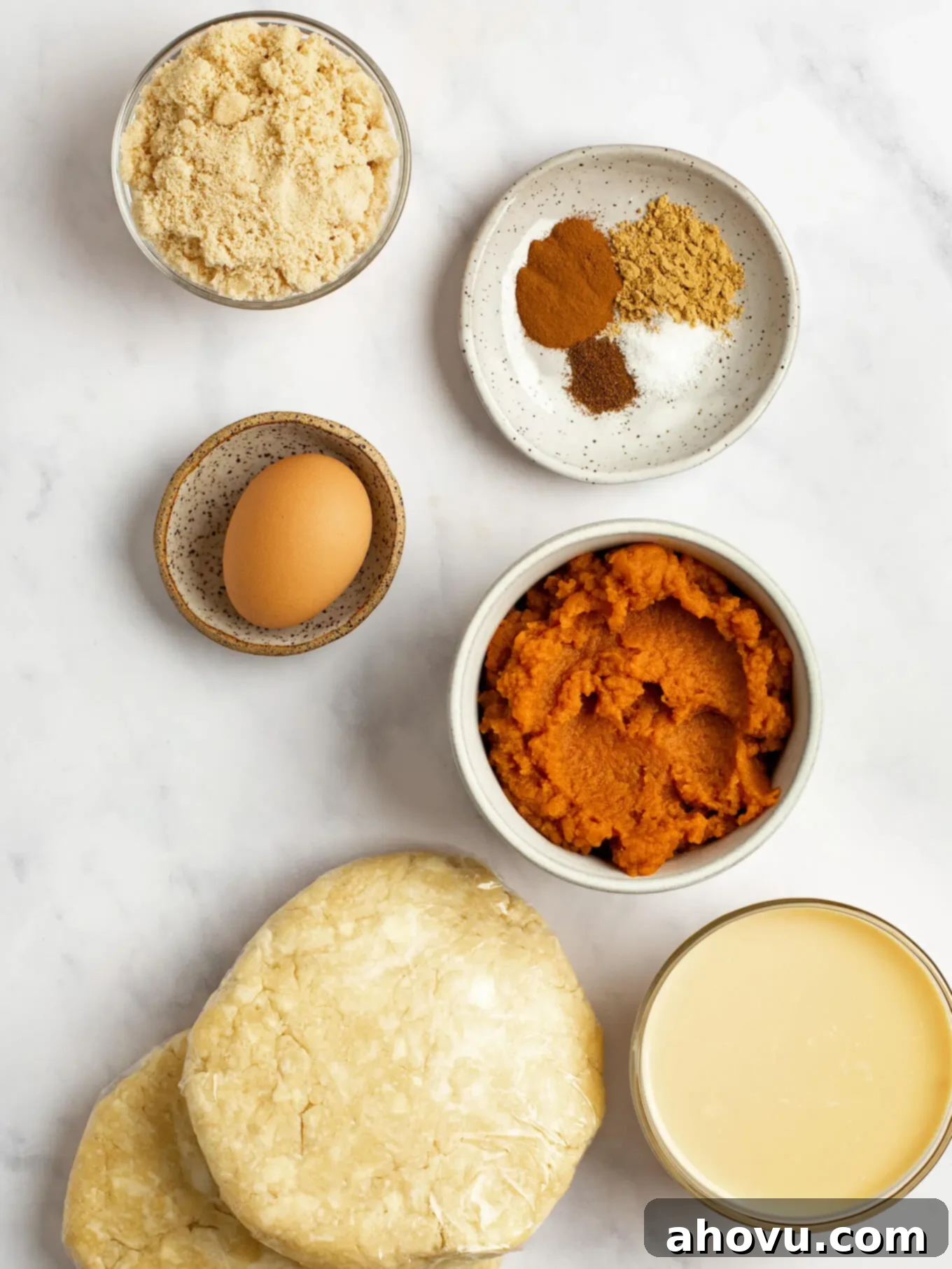 An overhead view of the ingredients for mini pumpkin pies on a marble surface.