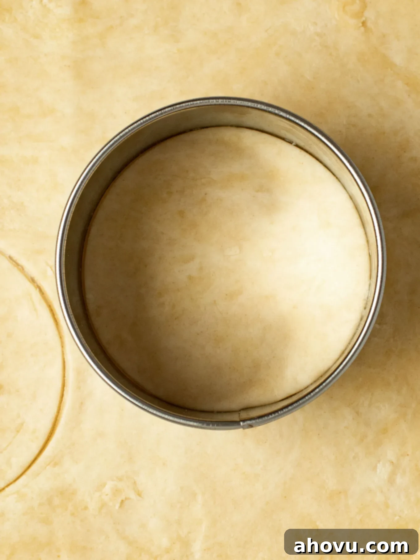 An overhead view of a pie crust that's been rolled out. A circular cookie cutter is cutting out a piece of the crust.