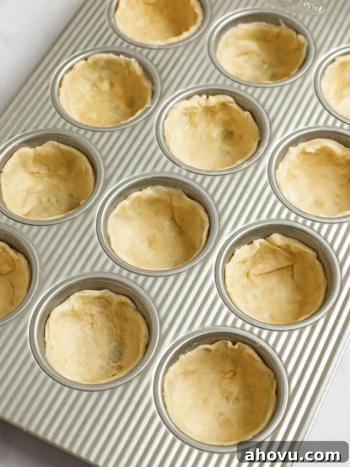 Circular pieces of pie crust pressed into a muffin pan.